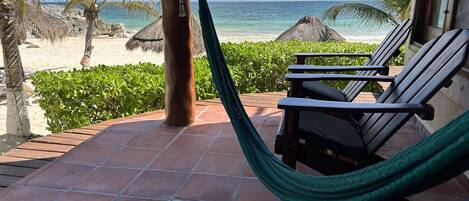 A terrace with a hammock, wooden chairs, and a view of a beach and ocean.