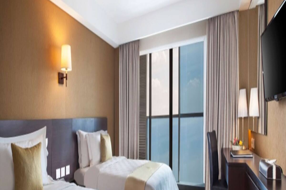 A hotel room with two beds, a desk, a chair, a TV, and a large window with curtains.