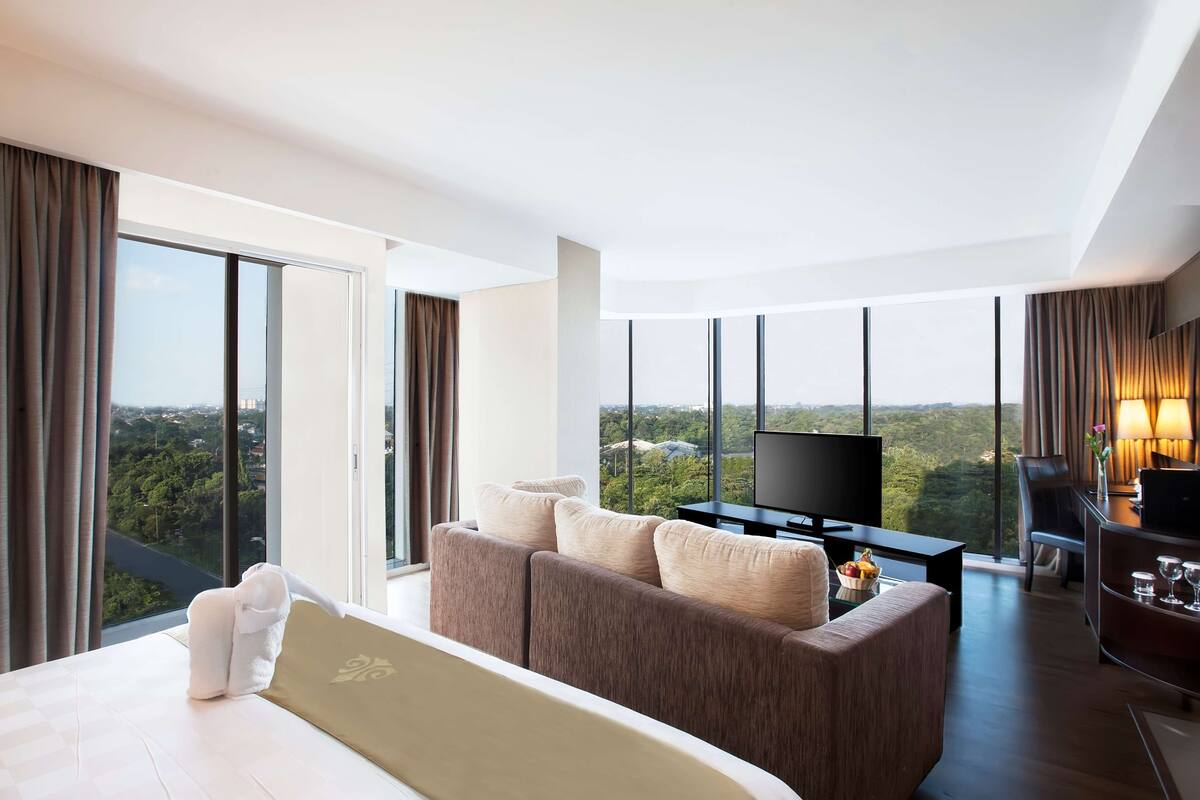 A modern hotel room with a large bed, a sofa, a TV, and a balcony with a city view.