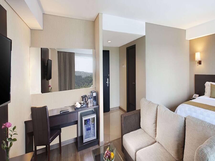 A hotel room with a bed, a sofa, a desk with a computer, a coffee machine, and a TV.