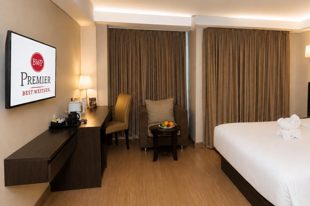 A hotel room with a bed, a desk with a lamp, a chair, and a painting on the wall.