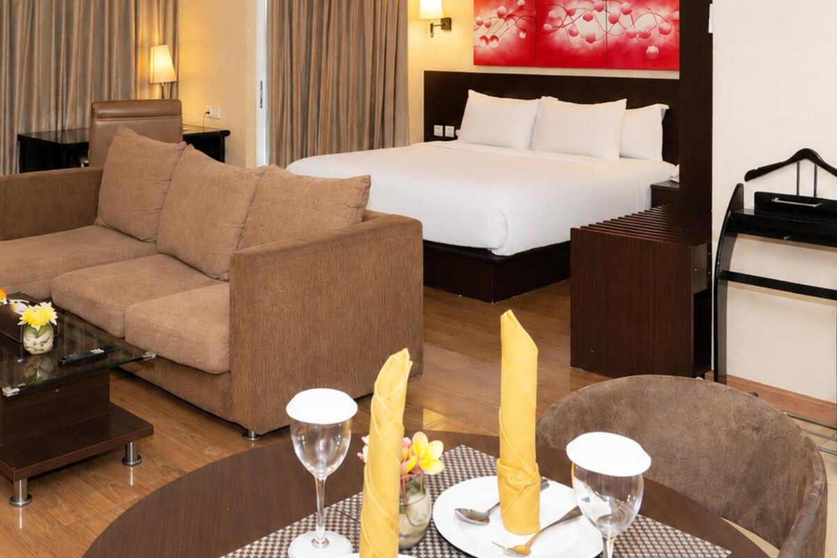 A hotel room with a sofa, a dining table with candles, a bed, and a nightstand.