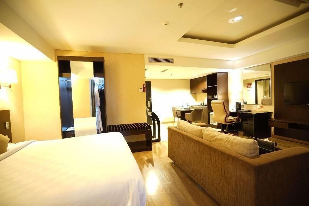 A hotel room with a bed, a sofa, a desk, and a television.