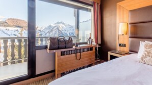 Habitación de hotel con un ventanal que ofrece vistas a la montaña, una mesita de noche de madera con una lámpara y una cama con un cojín estampado.