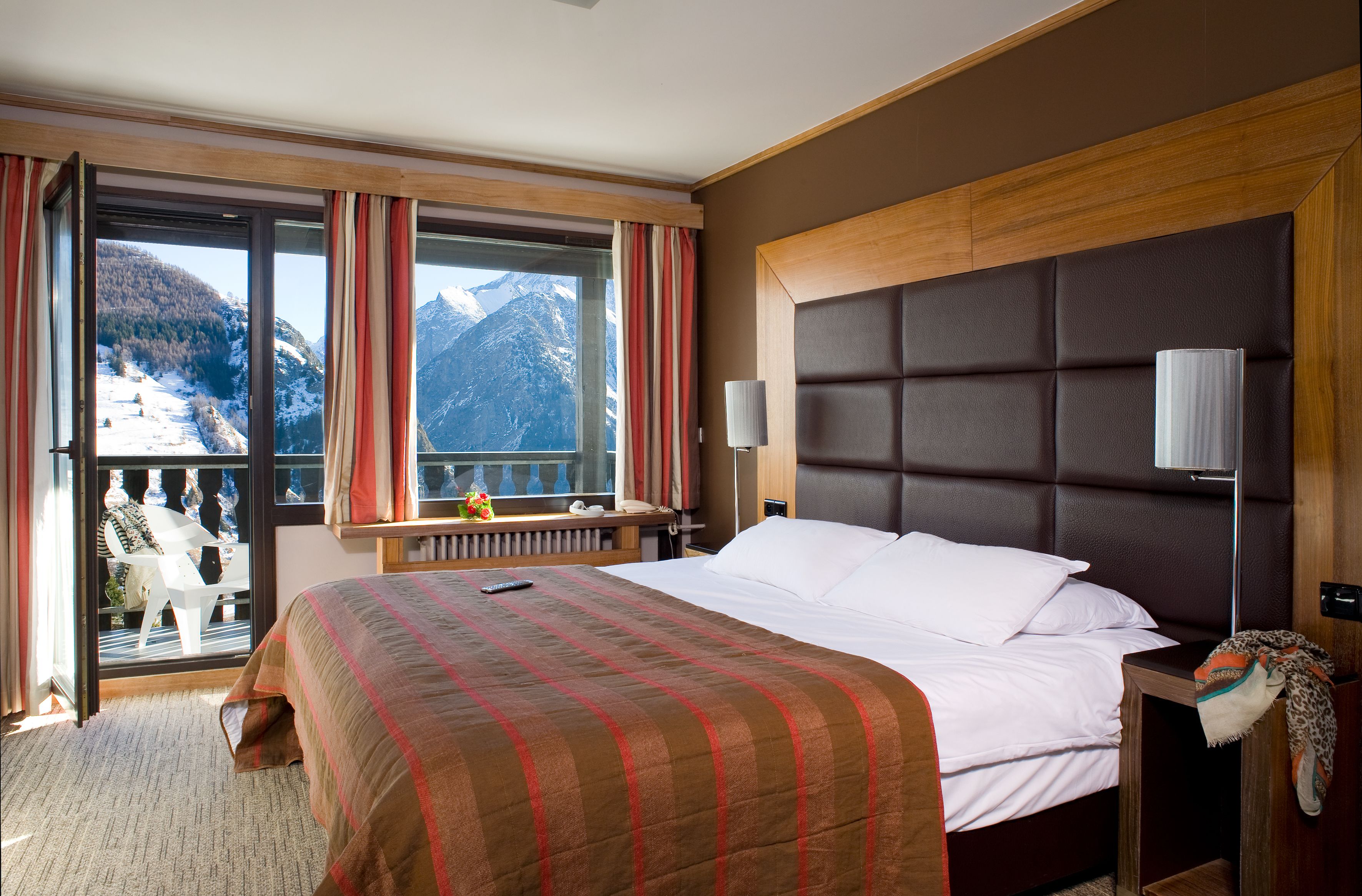 Ein Hotelzimmer mit einem großen Bett, Bergblick und einem Balkon mit einem Stuhl.