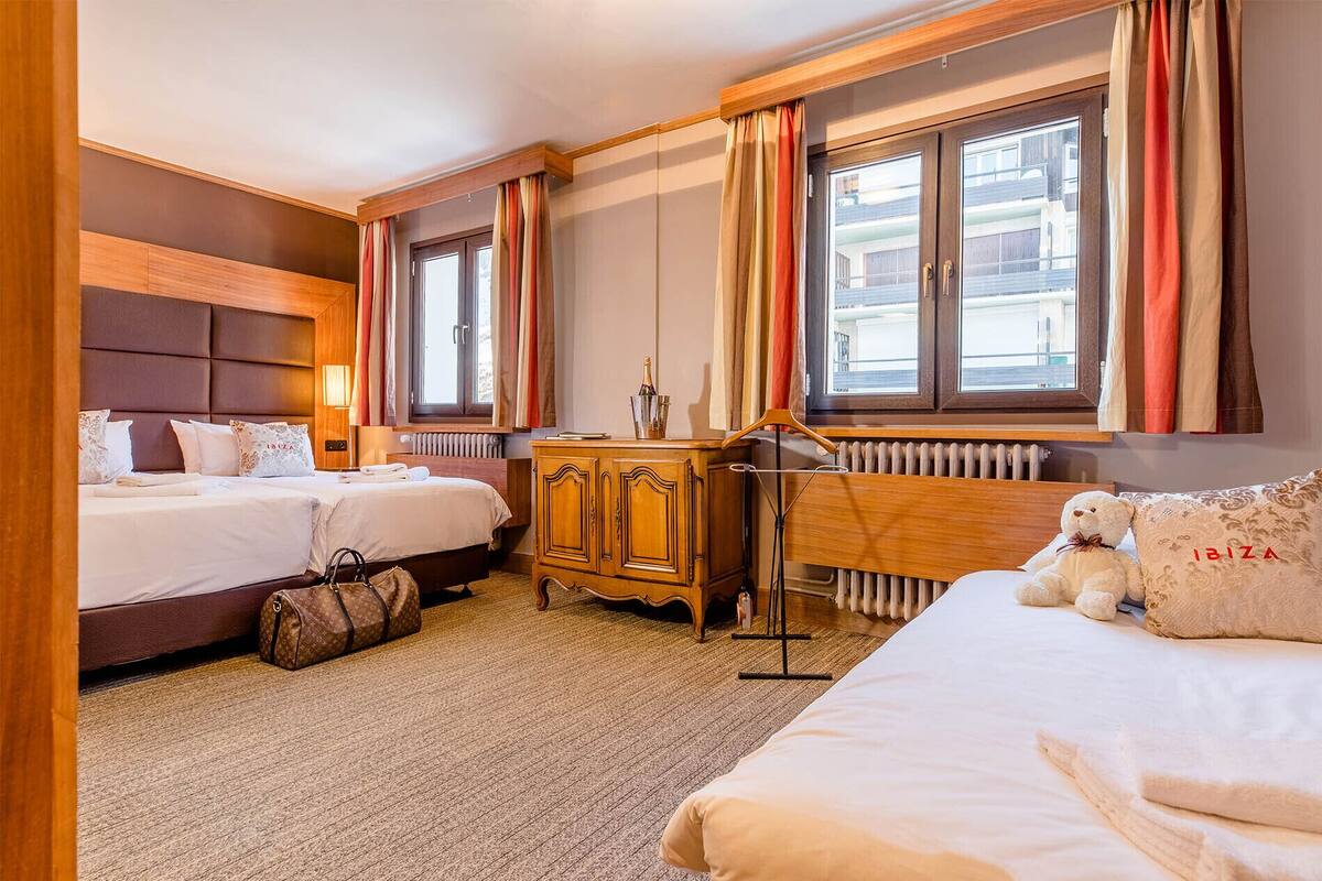 Une chambre d’h ôtel avec deux lits, une commode en bois, un radiateur et une fenêtre avec des rideaux.