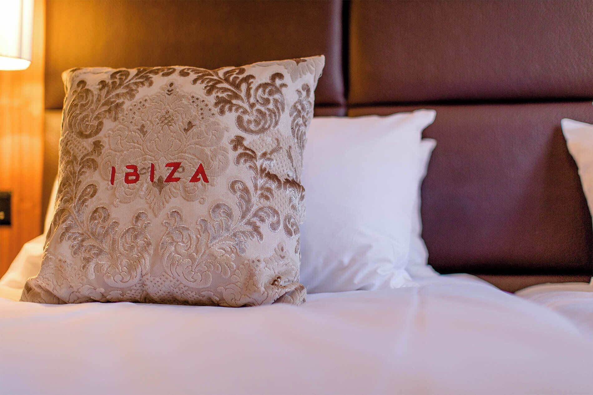 Una cama con un almohadón que dice "IBIZA" y un almohadón blanco sencillo.