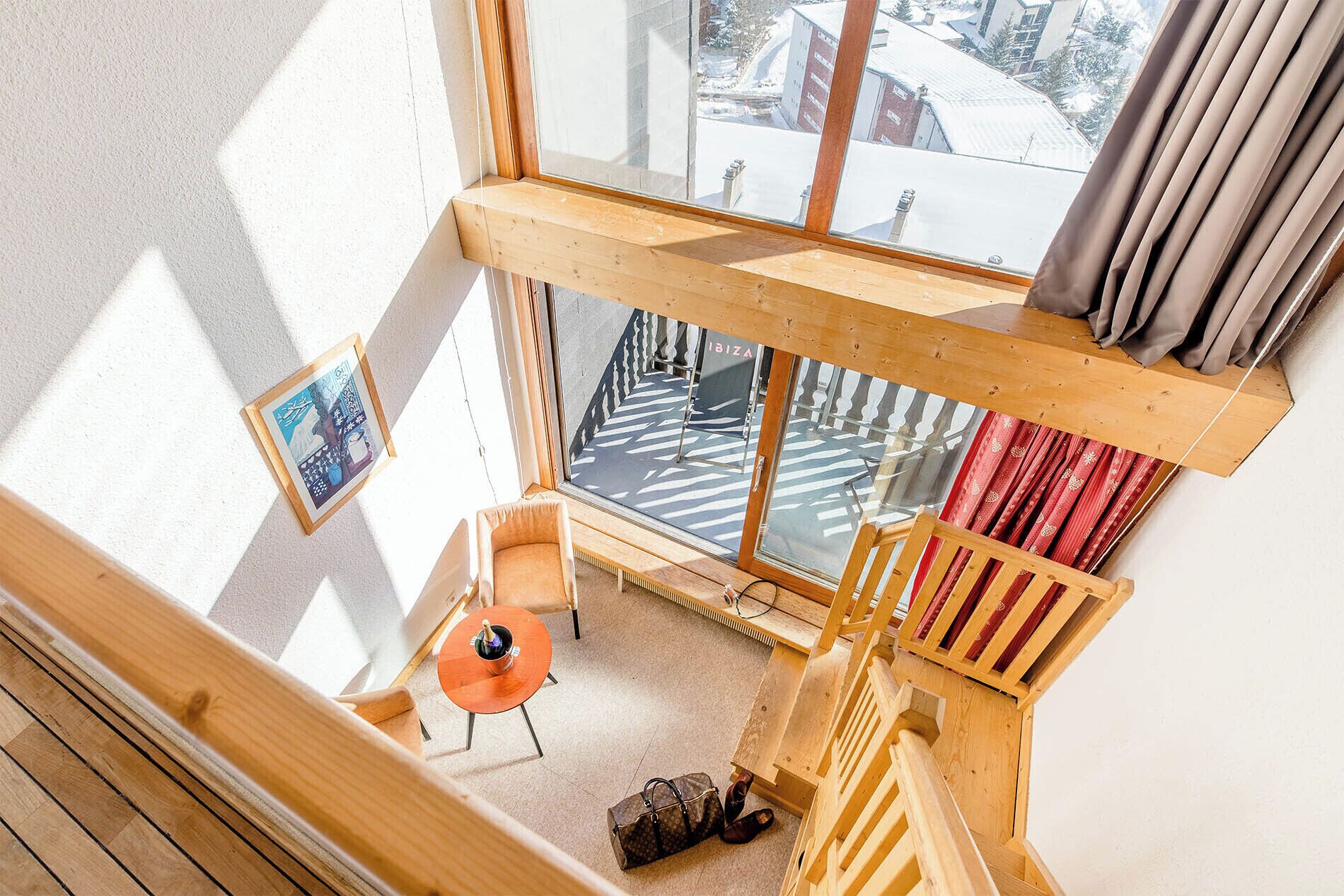 A corner room with a wooden bench, a small table, and a view of a snowy street through large windows.