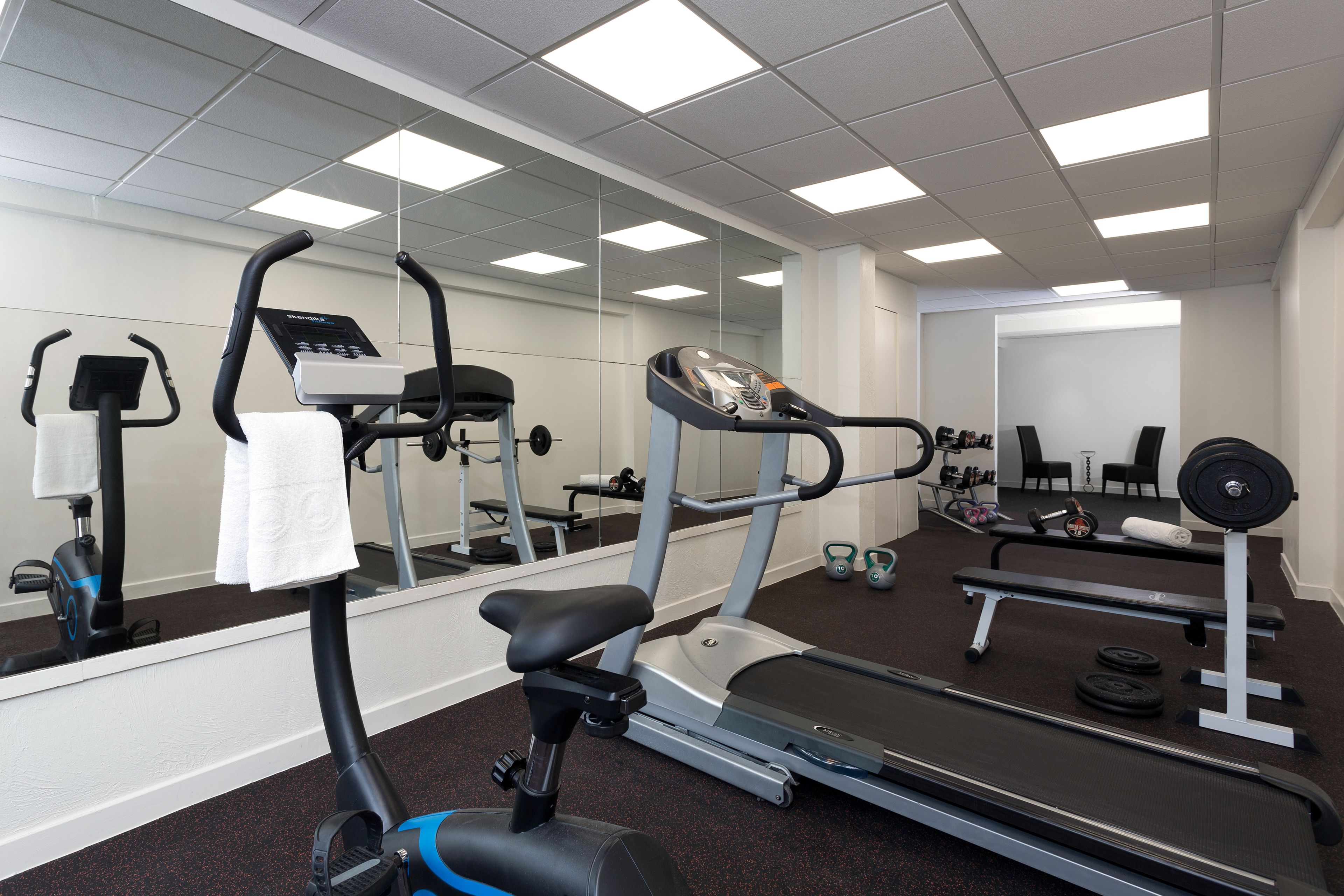 Un gimnasio con diversos equipos de ejercicio, incluyendo cintas de correr, una bicicleta estática y pesas.