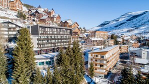 Un complejo de esquí con varios edificios, incluyendo un hotel moderno con balcones y una edificación de estilo chalé tradicional.