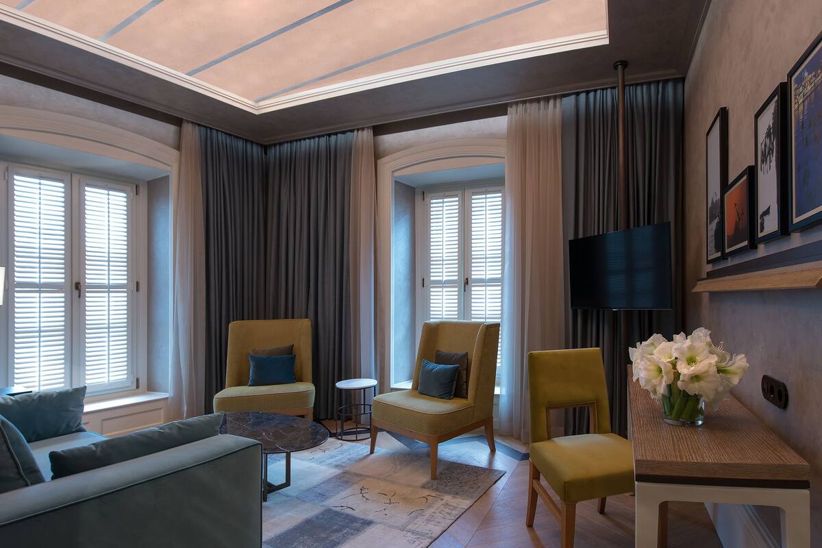 Une chambre d’hôtel moderne équipée d’un canapé, de fauteuils, d’une petite table et d’un téléviseur.