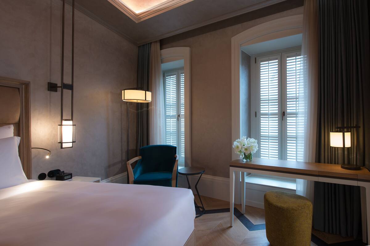 Une chambre d’hôtel avec un grand lit, un bureau avec une lampe, une chaise et une petite table.