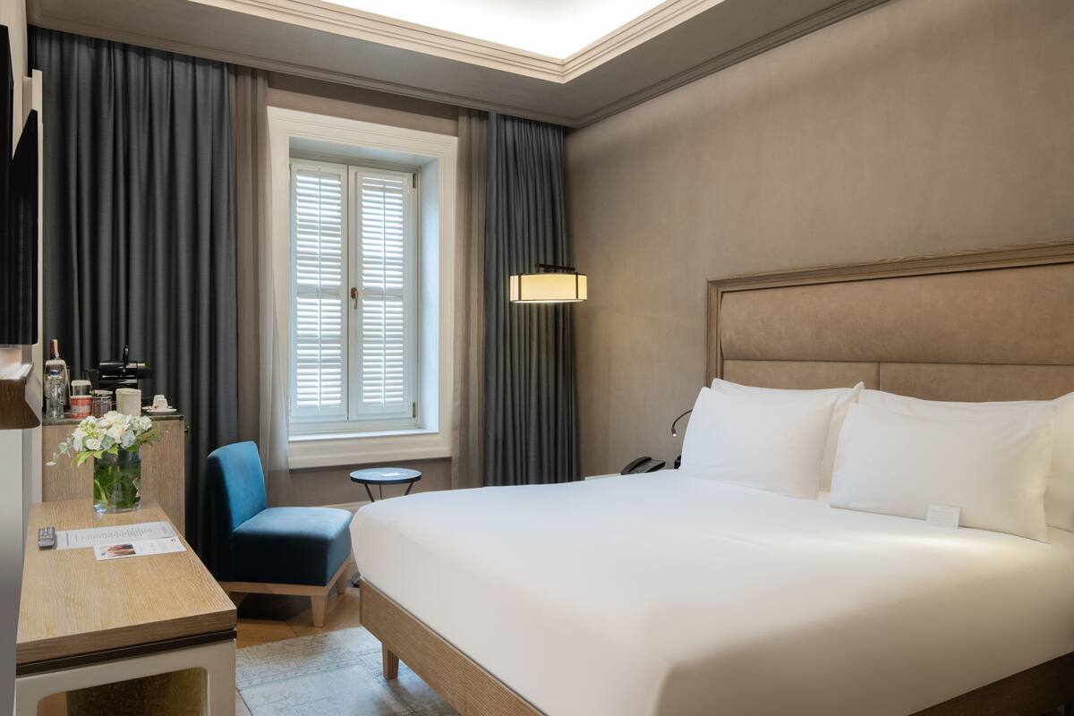 Une chambre d’hôtel avec un grand lit, un bureau avec une chaise, une petite table et une fenêtre avec des rideaux.