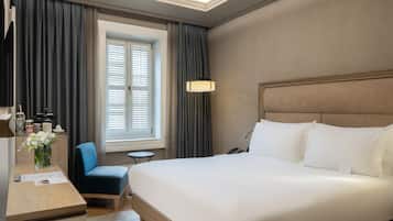 A hotel room with a large bed, a desk with a chair, a small table, and a window with curtains.