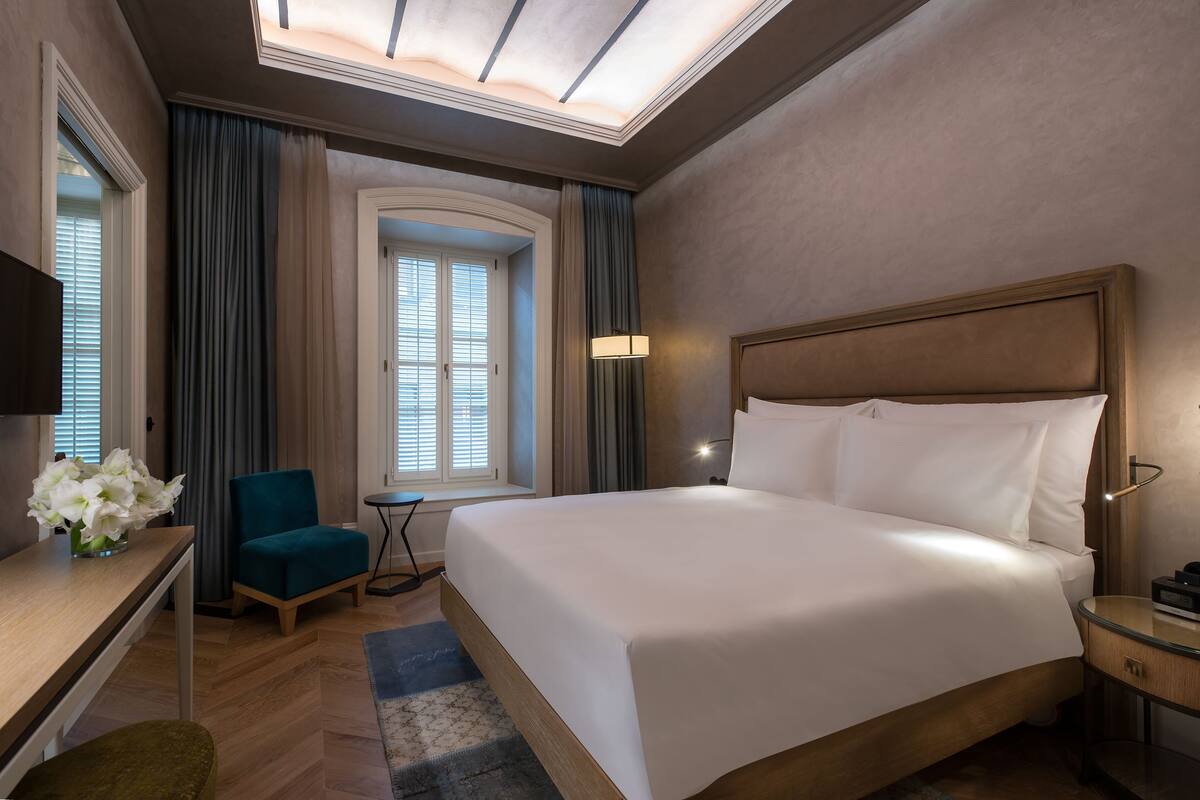 Une chambre d’hôtel avec un grand lit, un bureau avec une chaise, une petite table, un téléviseur et une fenêtre avec des rideaux.