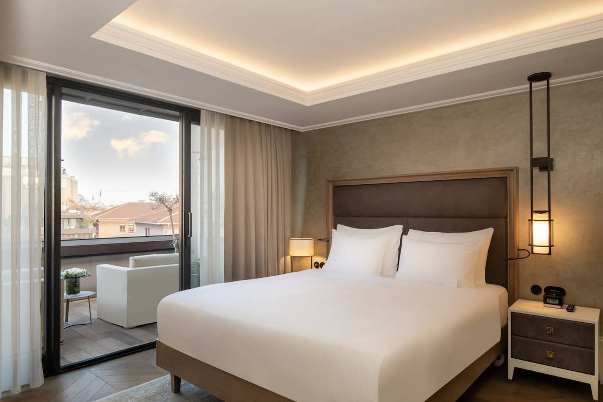 Une chambre d’hôtel avec un grand lit, une table de chevet, une lampe et une vue sur la ville, accessible par une porte coulissante.