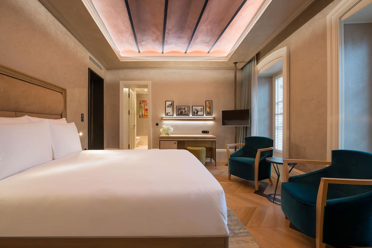 Une chambre d’hôtel avec un grand lit, un bureau, deux chaises, une télévision et des œuvres d’art accrochées au mur.