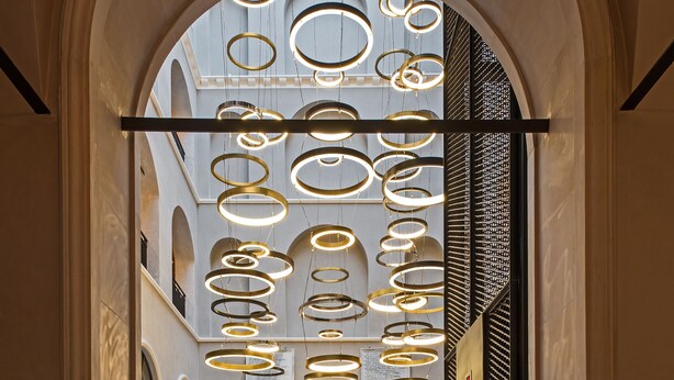 A grand hall with a high ceiling adorned with circular light fixtures, a central seating area with tables and chairs, and a view of the sky through an arched opening. - 10 Karakoy Istanbul - Special Class (Istanbul)