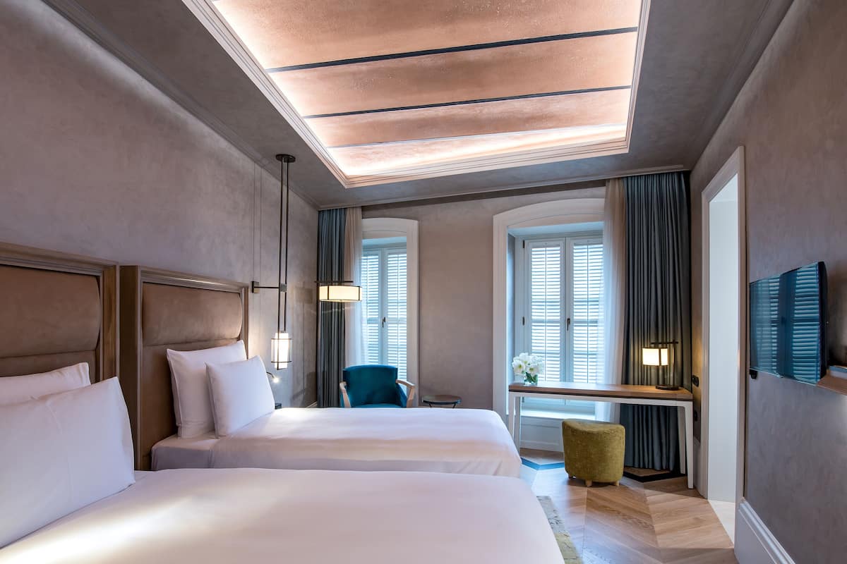 Une chambre d’hôtel avec deux lits, un bureau, une chaise et une petite table avec une lampe.