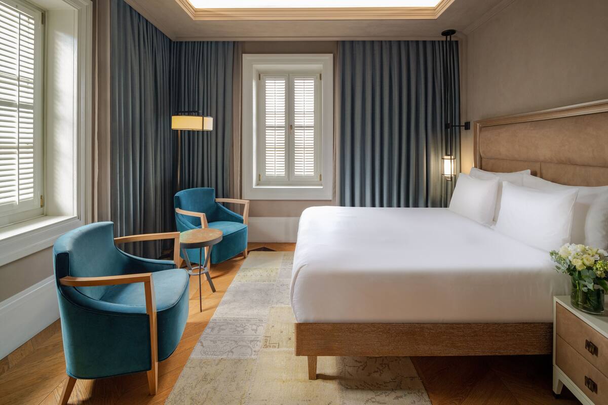 Une chambre d’hôtel avec un grand lit, un coin salon avec des fauteuils, une petite table et une fenêtre avec des rideaux.