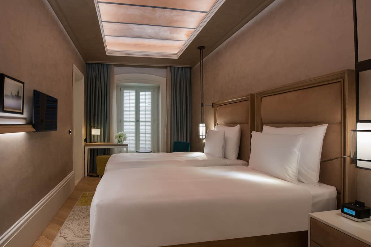 Une chambre d’hôtel avec deux lits, un bureau avec une lampe, une chaise et une table de chevet avec une horloge.