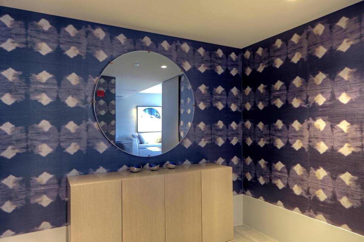 Un baño con espejo redondo, papel tapiz estampado y tocador de madera.