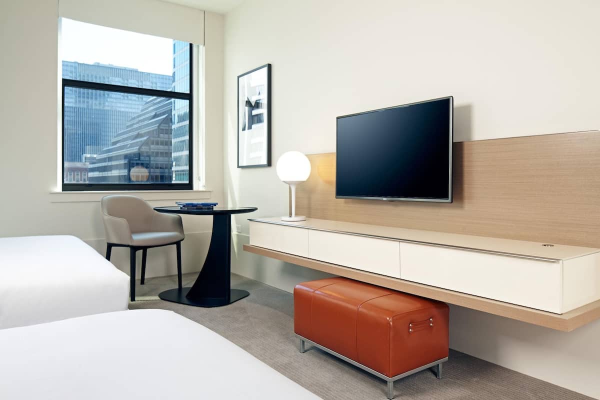 Una habitación de hotel con una cama, un escritorio con computadora, una silla, un televisor y una ventana con vista a la ciudad.
