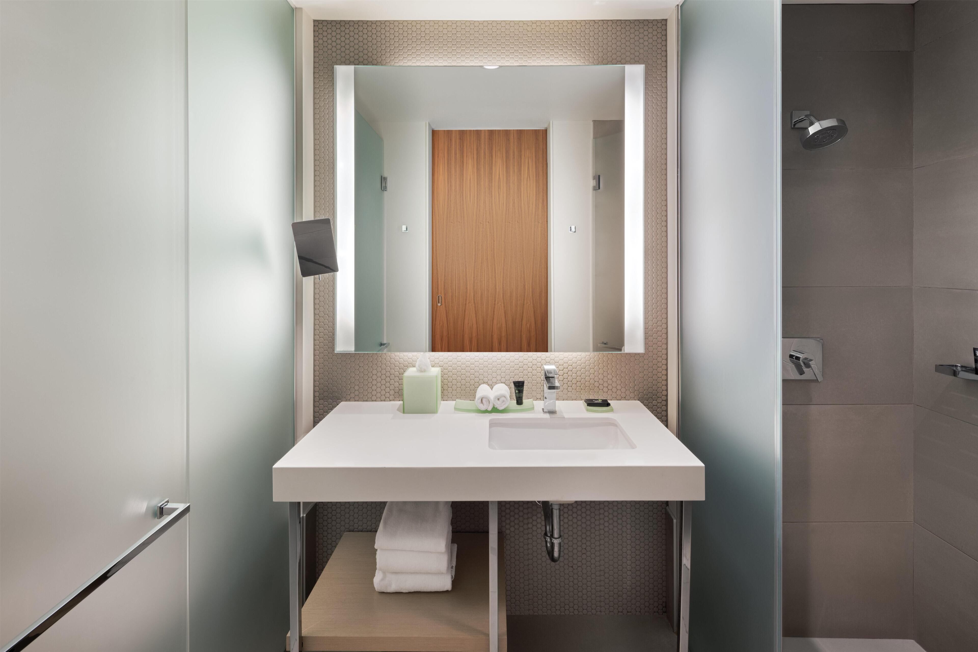 Un baño moderno con un espejo grande, lavamanos blanco y zona de ducha.