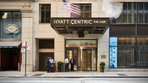 The exterior of the Hyatt Centric The Loop hotel with a prominent American flag, a classic facade, and a glass entrance.