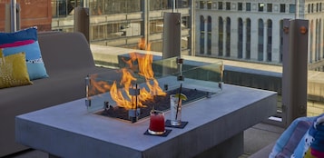 Un espace extérieur moderne, aménagé avec des sièges confortables, une table à plateau de verre, un foyer et une boisson.