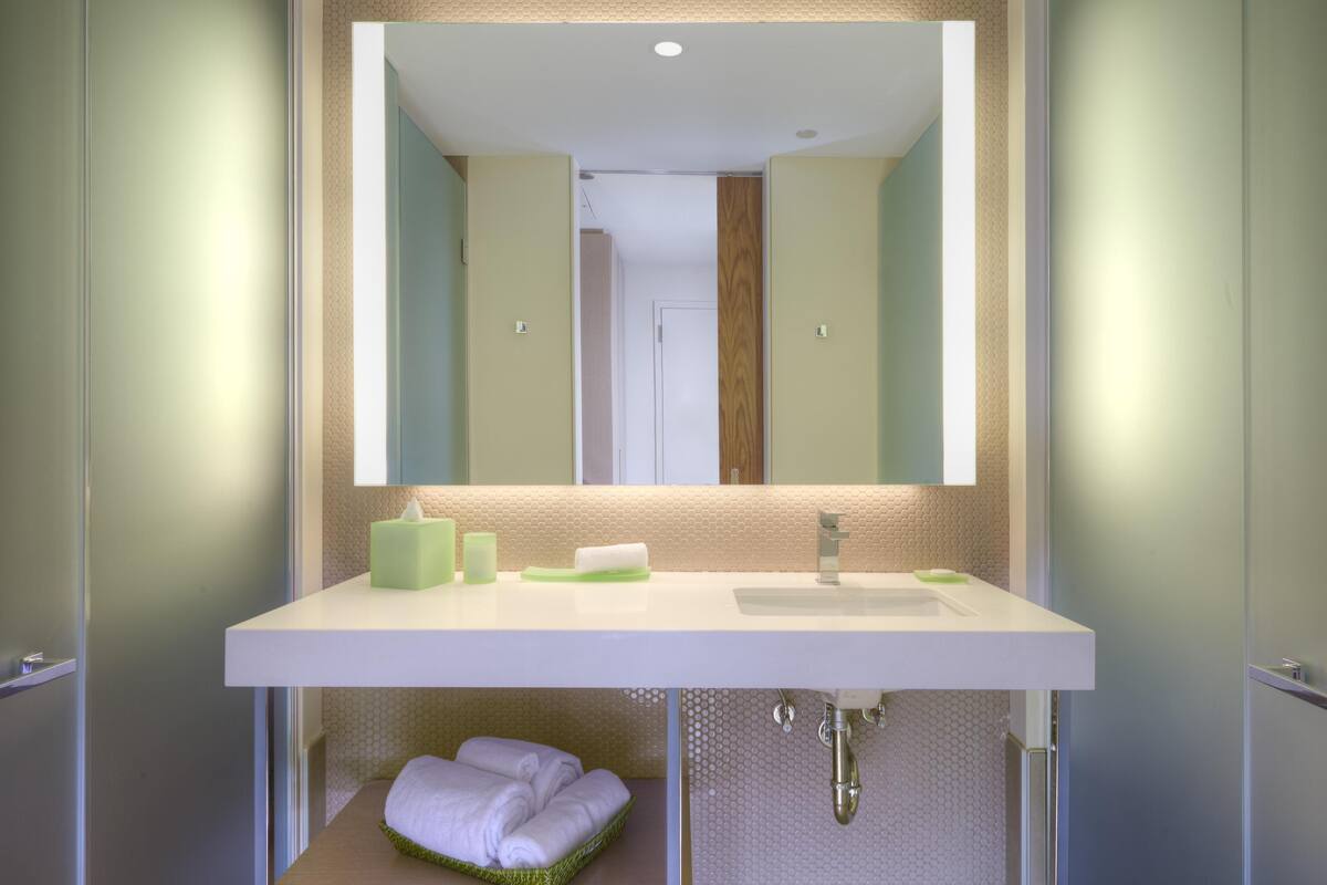 Un baño con lavamanos blanco, espejo y toallero.