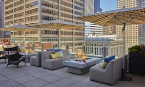 A rooftop terrace with outdoor seating, fire pits, and umbrellas.