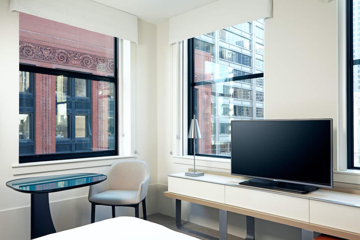 Habitación de hotel moderna con un ventanal grande, un televisor de pantalla plana, una mesita y una silla.