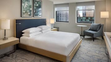 A hotel room with a bed, two bedside lamps, a chair, a small table, and artwork on the wall.