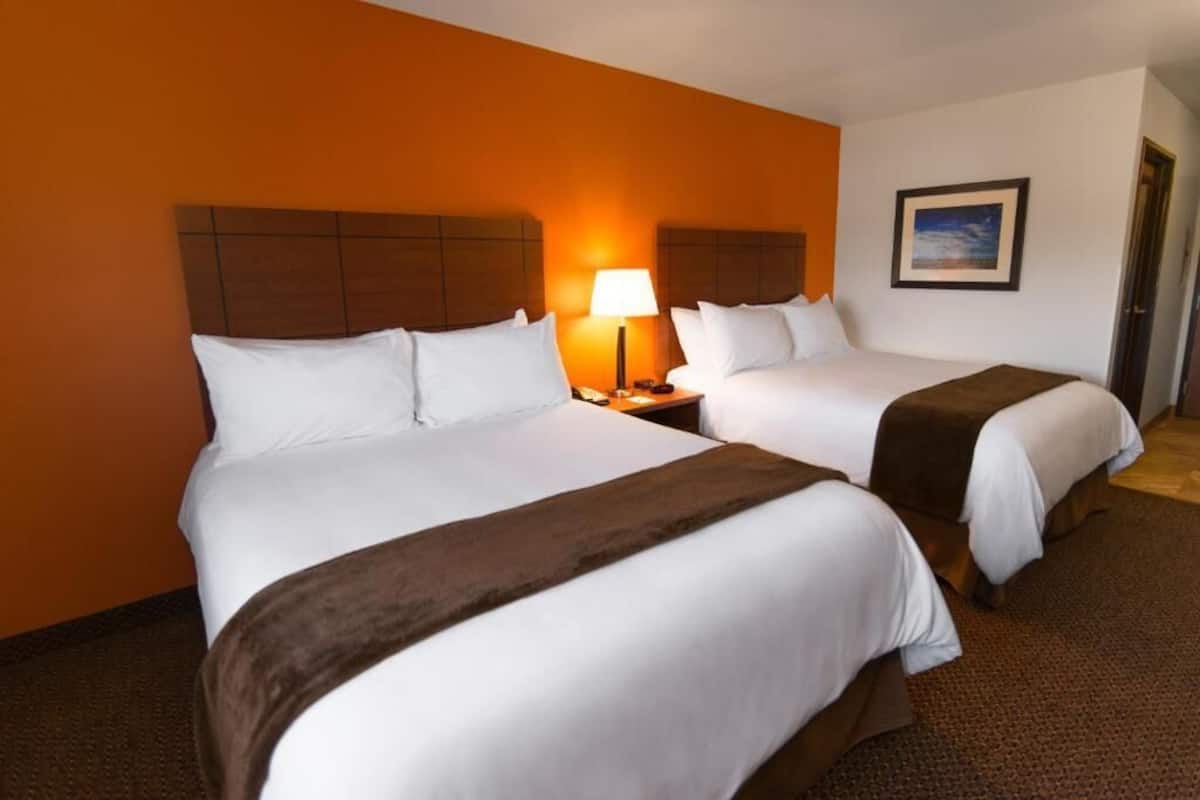 A hotel room with two beds, a nightstand with a lamp, and a framed picture on the wall.