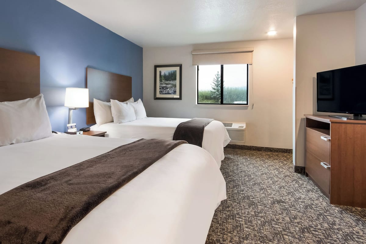A hotel room with two beds, a television, a desk, and a window with a view of trees.