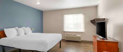 A hotel room with a bed, a desk, a television, and a window with blinds.