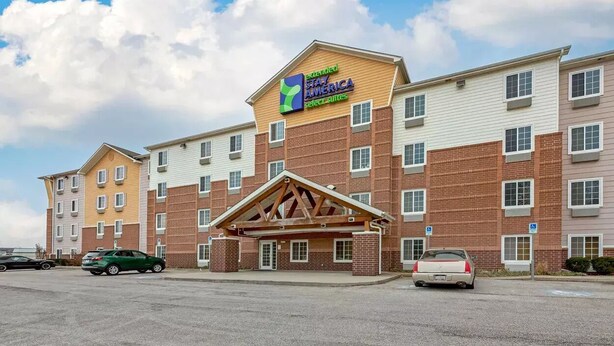 Ein Hotel mit zentralem Eingang, mehreren Etagen und einem Parkplatz.