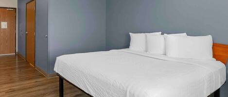 A hotel room with a large bed, a wooden floor, and a blue wall.