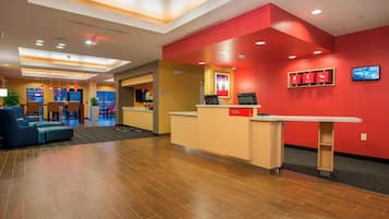 A hotel reception area with a red accent wall, a reception desk, and a seating area with blue sofas.