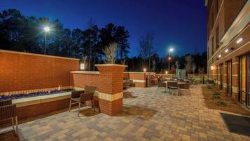 An outdoor patio area with brick flooring, seating, and a fire feature.