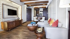 A modern living room with a stone accent wall, wooden beams, a flat-screen TV, a white sofa with red cushions, and a wooden coffee table with magazines.