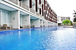 A swimming pool adjacent to a multi-story hotel with balconies and a view of another building.