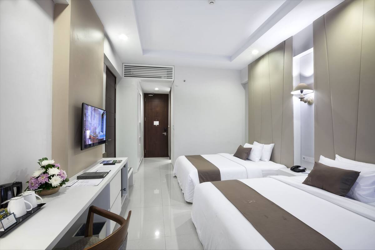 Ein Hotelzimmer mit zwei Betten, einem Schreibtisch mit Computer, einem Fernseher und einer Badezimmertür.