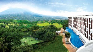 A hotel with a pool, surrounded by lush greenery and a view of a distant mountain.