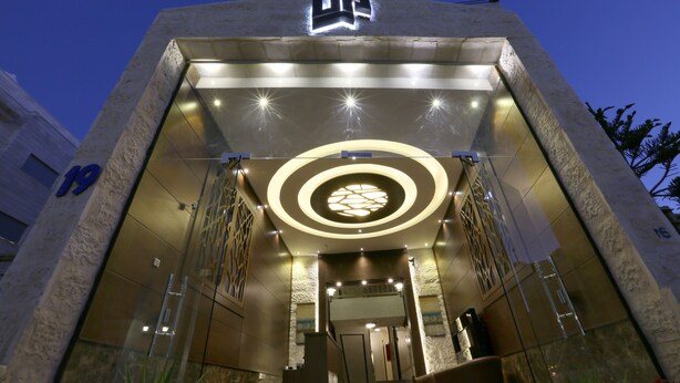 A modern building entrance with a prominent circular light fixture, a staircase leading to the entrance, and a visible number '19' on the left.
