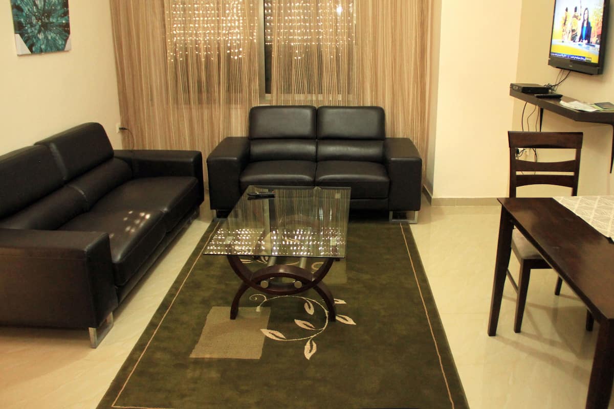 Una sala de estar con un sofá, una mesa de centro de vidrio, una mesa de comedor y un televisor.
