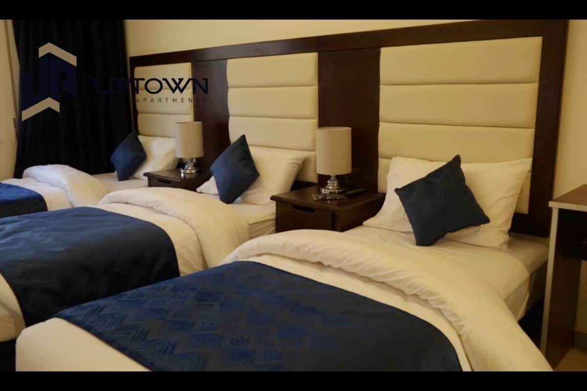 Habitación de hotel con dos camas, cada una con cabecero, mesitas de noche, lámparas y almohadas.