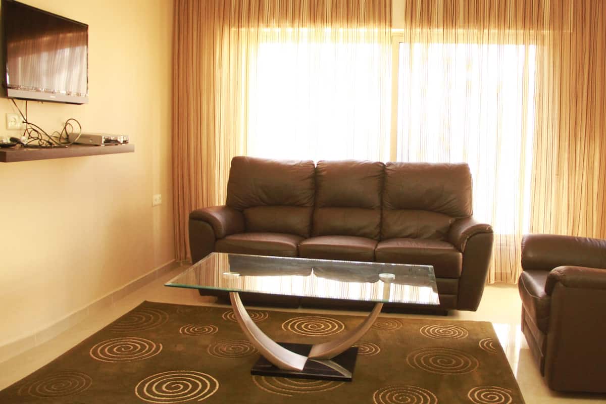 Una sala de estar con un sofá de cuero marrón, una mesa de centro de vidrio, un sillón marrón y una alfombra estampada.