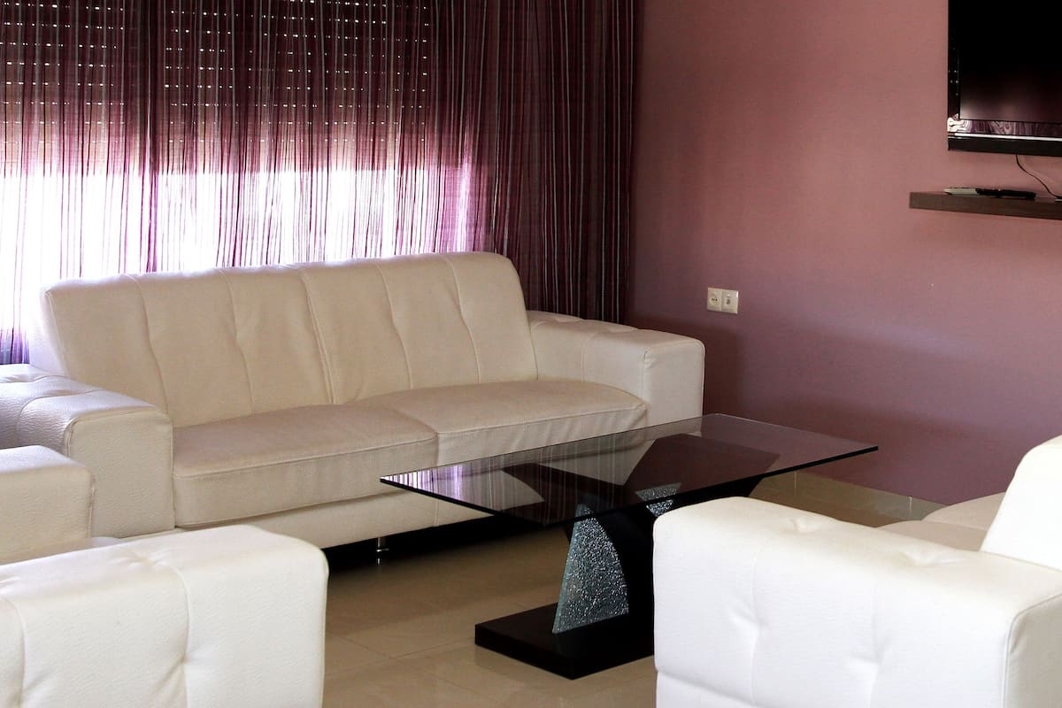 Una sala de estar con un sofá blanco, una mesa de centro de vidrio y un televisor montado en la pared.